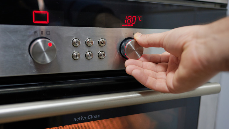 Hand of an unrecognizable person using the temperature selector of an oven in the kitchen of his home to preheat and then bake.