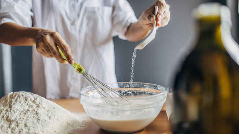 A young woman pours salt in a glass container with milk, she prepares the dough