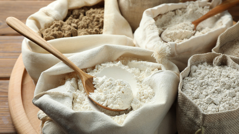 Different types of flour in bags on wooden table, closeup