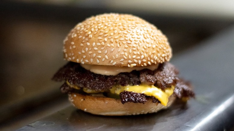Cheeeseburger with seeded bun sitting on grill at Amboy Quality Meats & Delicious Burgers