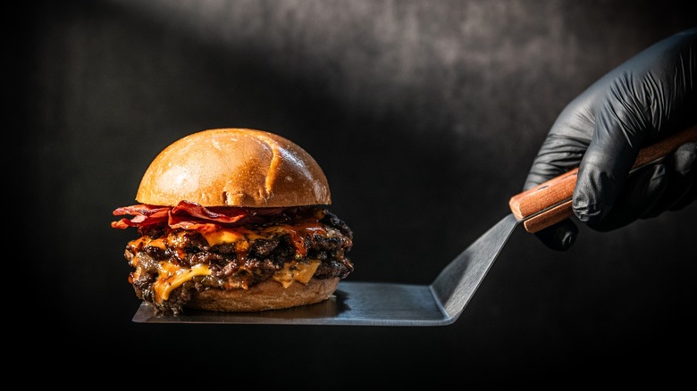 Gourmet Double Smash Burger with Crispy Bacon and Melted Cheese on a Spatula