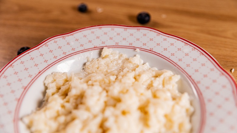 Close-up of creamy rice pudding porridge served in a patterned bowl on a wooden table, with a few scattered blueberries surrounding