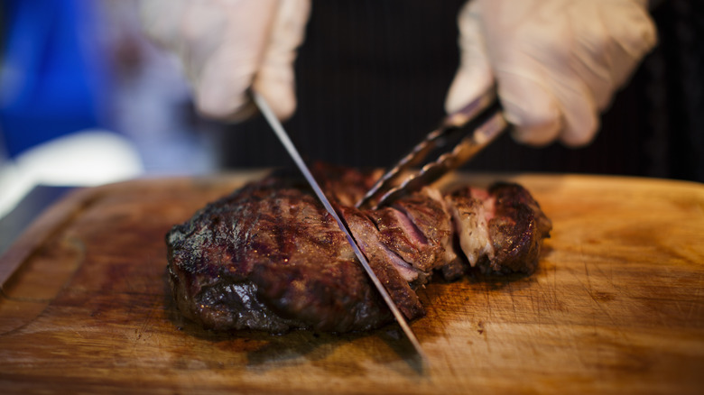 Gloved hands cutting steak