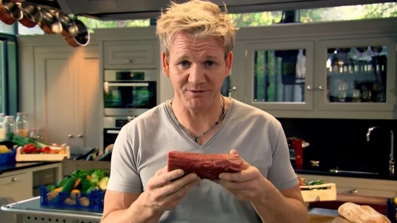 Gordon Ramsay holding a steak in a kitchen