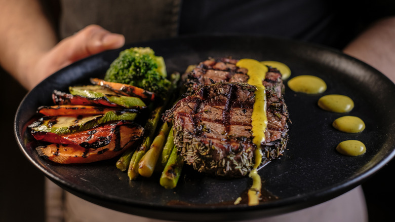 Hands holding plate with vegetables and steak