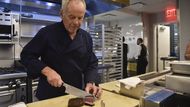 Wolfgang Puck cutting a steak in the back of a restaurant kitchen