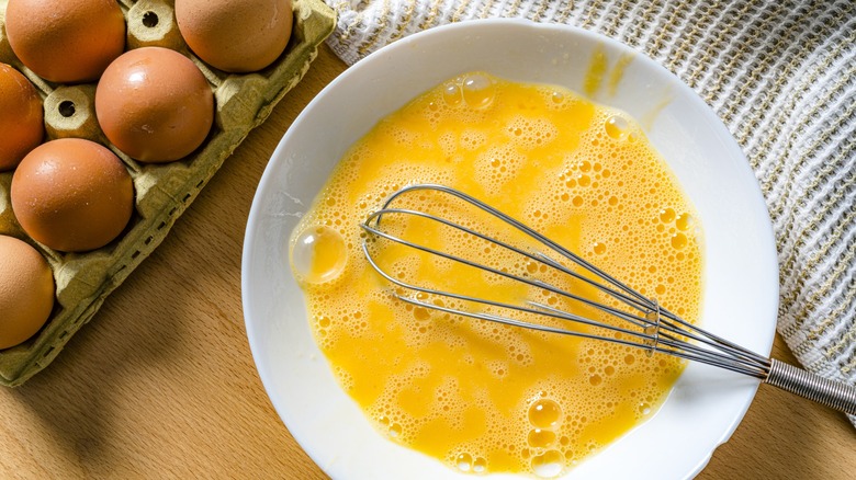 Overhead shot of scrambled raw eggs in a white bowl.