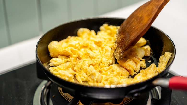 Chef shown removing scrambled eggs from heat on stove