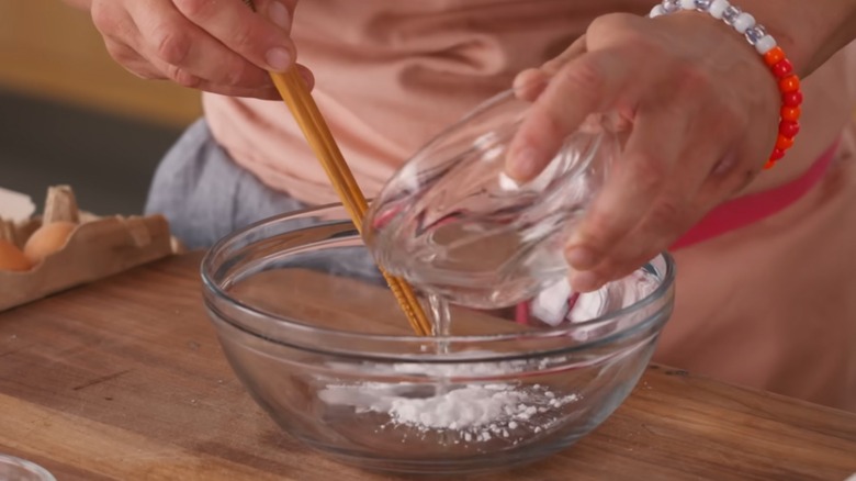 Chef hand shown creating a cornstarch slurry in a glass bowl and stirring it
