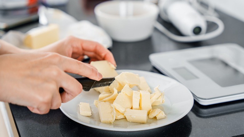 Hands slice cold butter into small pieces or cubes
