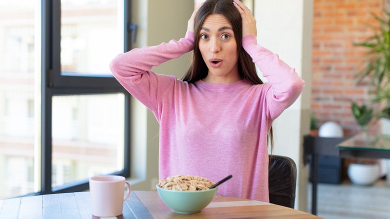 Young caucasian woman sitting in front of a bowl of cereal with shocked facial expression on her face