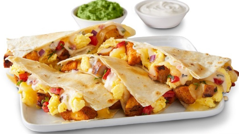 Qdoba Breakfast Quesadilla on a rectangular white plate in front of small white bowls filled with guacamole and sour cream on a white background.