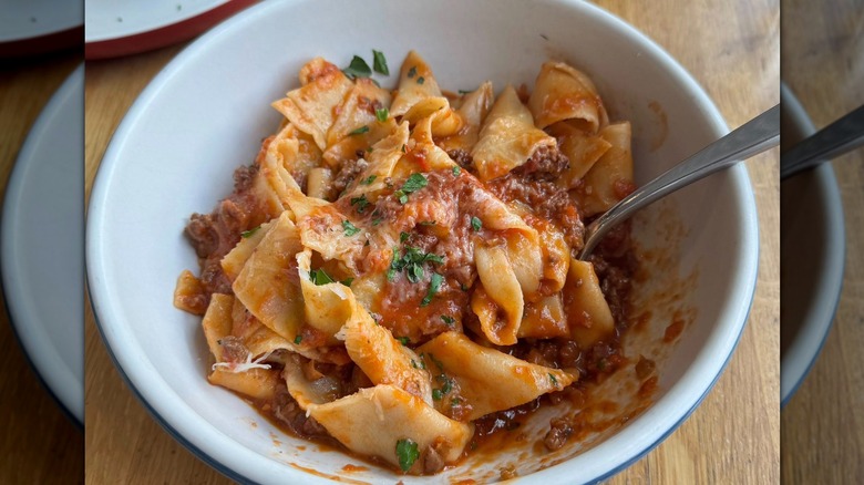 wide flat noodles with bolognese and herb garnish in bowl with utensil at North Italia