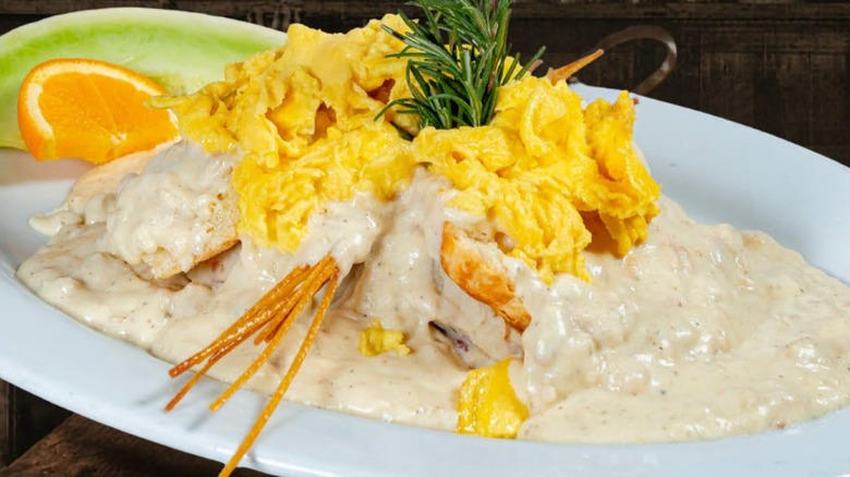 Biscuits and gravy topped with scrambled eggs and a side of fresh fruit at Hash House A Go Go