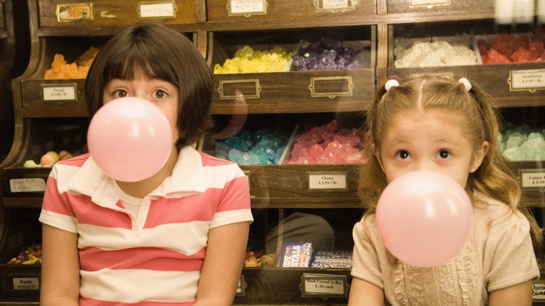 two kids seeming from earlier days like the 1990s, at a candy store, blowing bubble gum bubbles