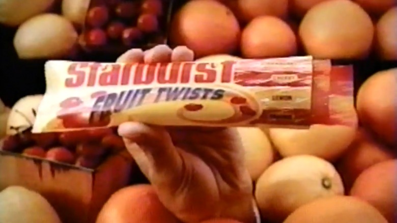 Hand reaching up out of a pile of oranges holding a Starburst Fruit Twists packet