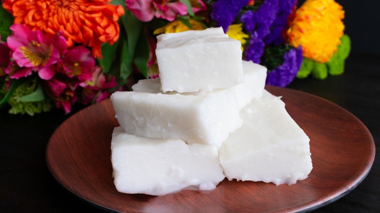 Stacked cubes of coconut pudding on a wooden plate with brightly colored flowers