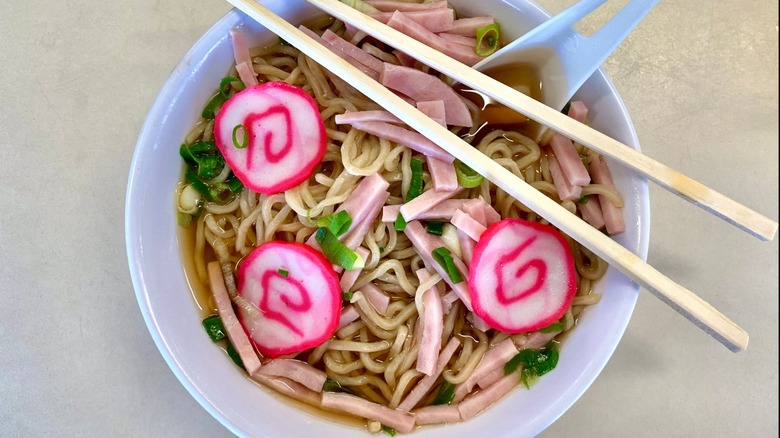Saimin Hawaiian ramen noodles with Spam and Narutomaki fish roll, in a white bowl with chopsticks