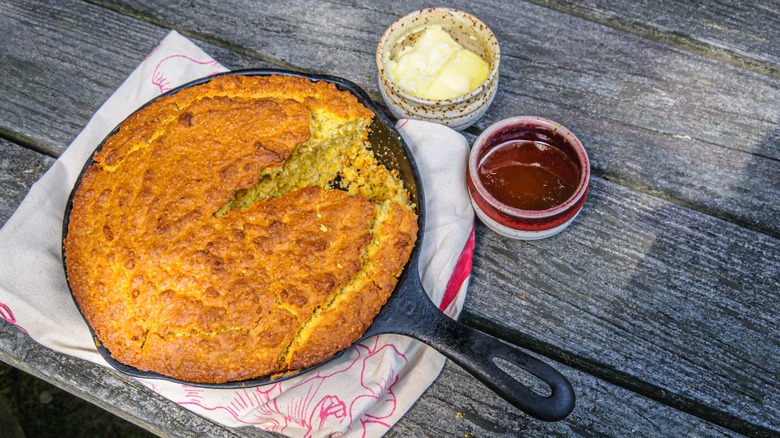 Fresh cornbread, baked in an old cast iron skillet, is served warm with creamy butter and honey on an old outside wooden picnic table