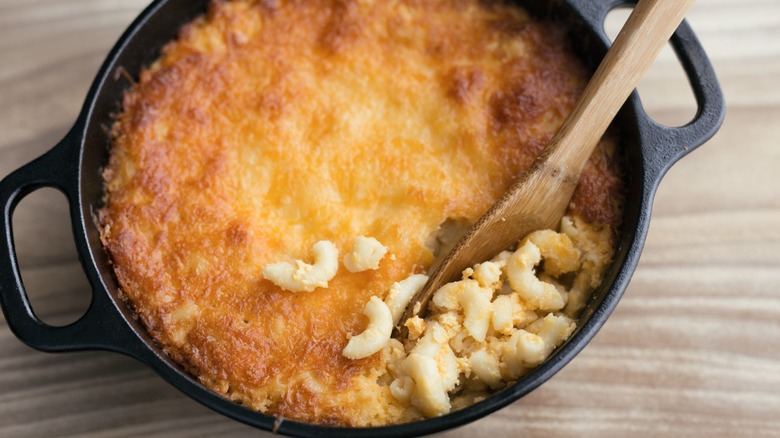 Southern style macaroni and cheese in a cast iron skillet being scooped out with a wooden spoon