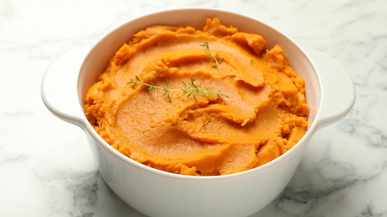 Mashed sweet potatoes in a white pot on a white marble table