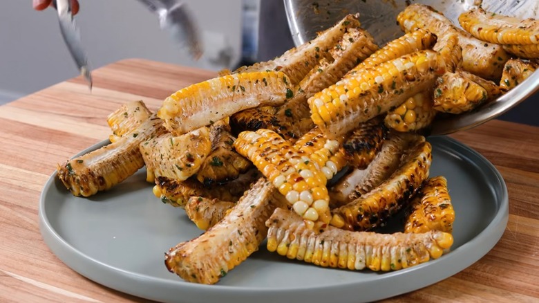 Cowboy Butter Corn ribs being plated on a serving platter by a chef with silver tongs