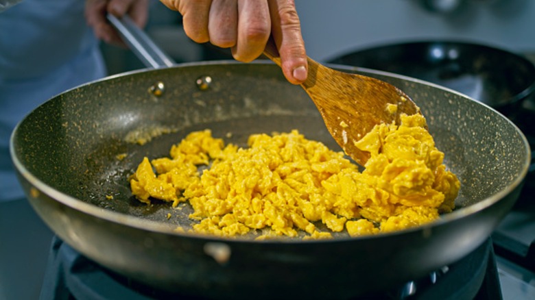 hand preparing scrambled eggs in a pan