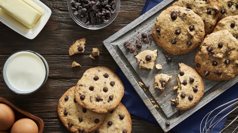 chocolate chip cookies on a counter with milk, butter, eggs, and chocolate chips