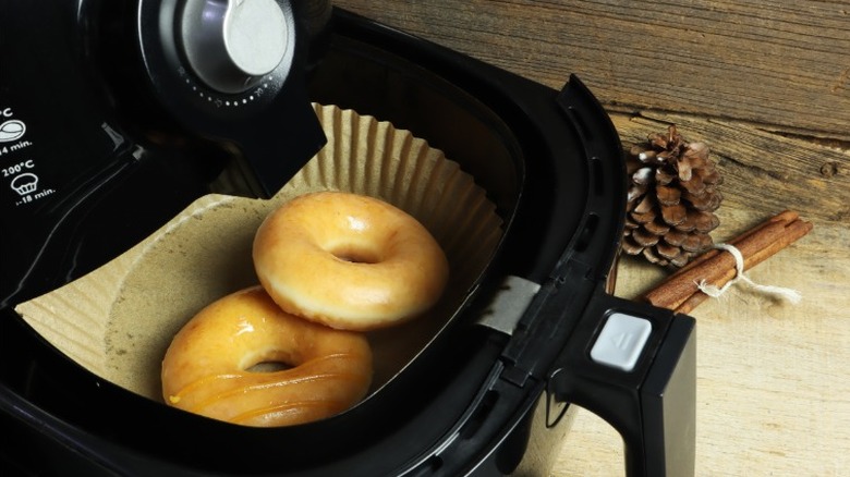 two glazed ring donuts sit in an air fryer on a wood surface