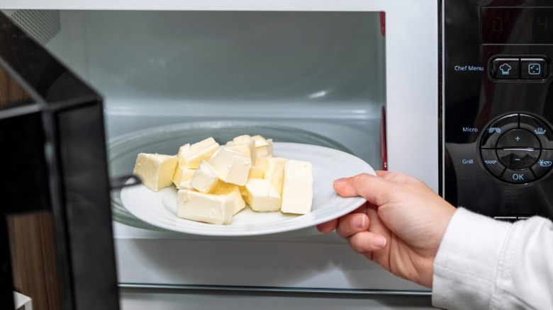 a hand puts a plate of butter cubes into a microwave