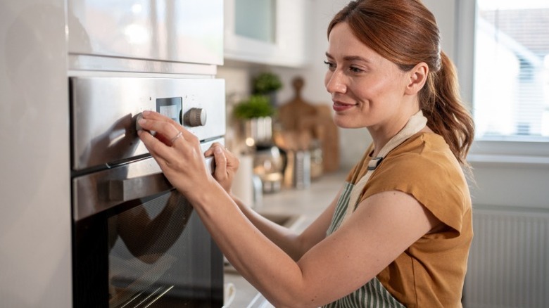 a woman in an apron turns a knob on the oven in her kitchen