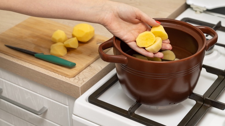 Person adding adding peeled potatoes to an earthenware pot
