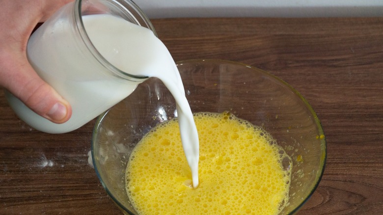 Adding milk into into whisked eggs in a glass bowl