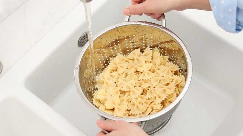 Pasta being rinsed in a colander in the kitchen sink
