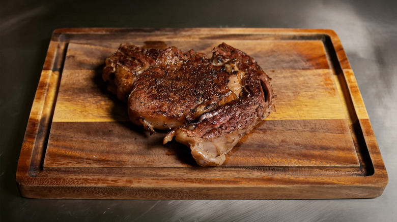 Grilled beef steak resting on wooden cutting board, seasoned and cooked with seared crust