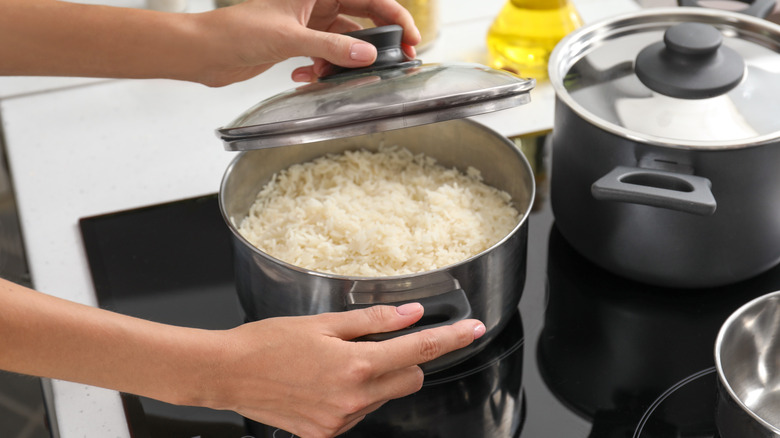 Woman removing cover off of a pot of rice on stove in kitchen