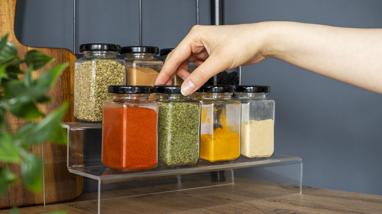 Cropped hand selecting jar of herbs on a spice rack with other jars in kitchen