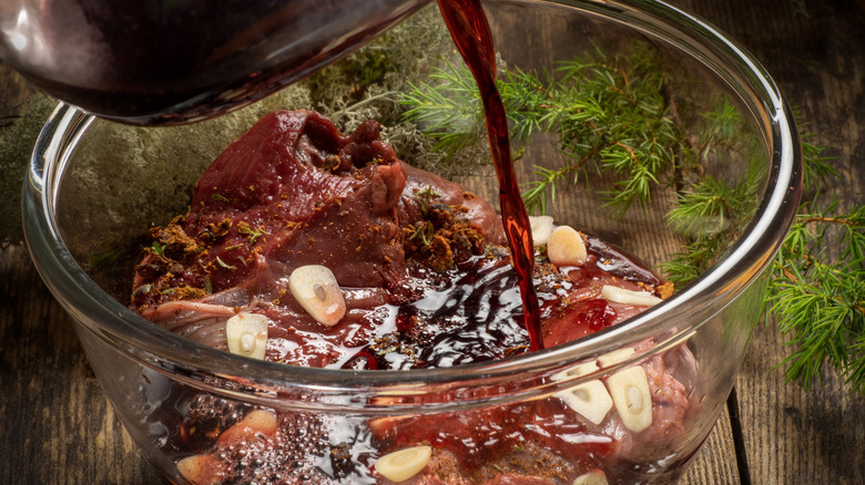 Red wine poured into bowl of fresh game meat marinating in garlic and herbs