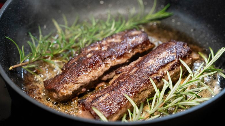 Strips of venison and herbs frying in pan