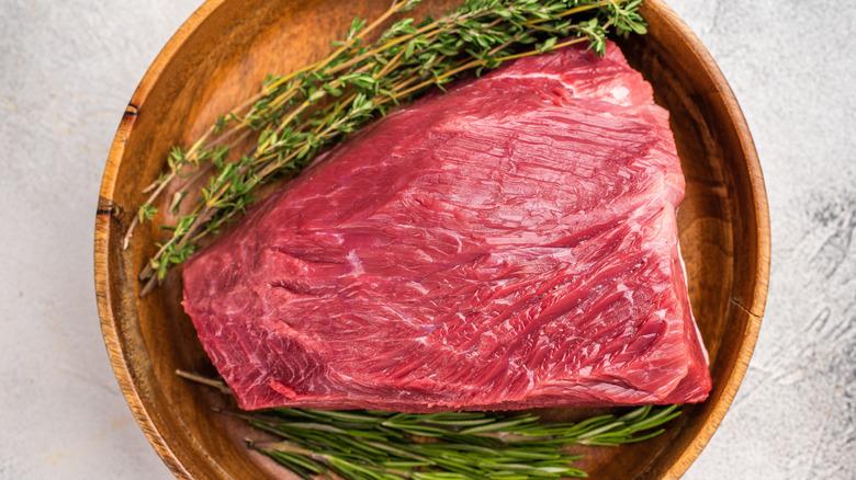 Raw chunk of deer meat on wooden plate with fresh herbs
