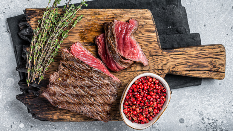 Grilled slices of venison on wooden cutting board with herbs and spices