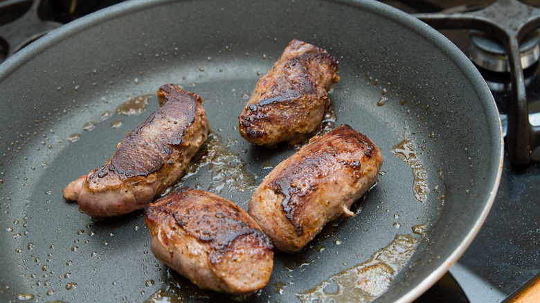 Four cuts of venison searing in a frying pan