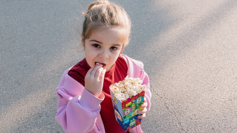 Cute girl toddler eating popcorn from bucket with Labubu design as a snack