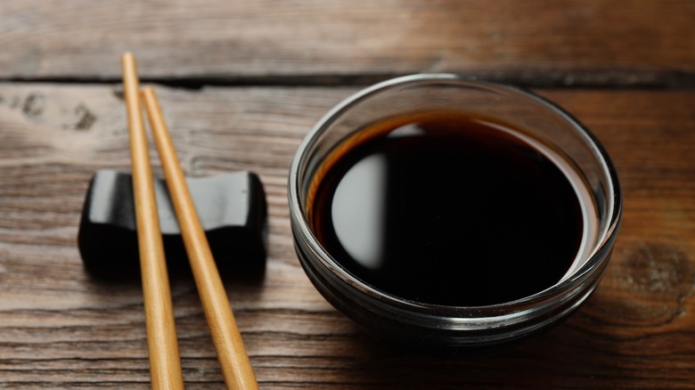 Soy sauce in a glass bowl with chopsticks on the side on a wooden table
