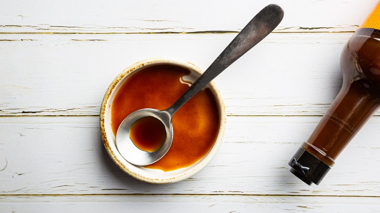 Worcestershire sauce in a bowl with spoon and bottle leaned on its side