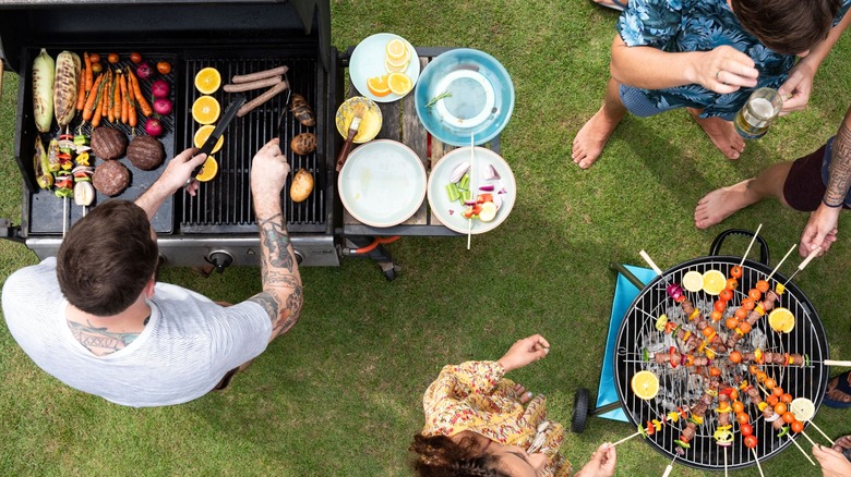 Top view of people grilling various foods on two grills in a backyard