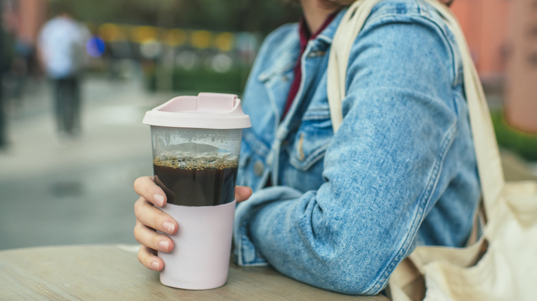 Someone holding a reusable cup that is sitting on a table