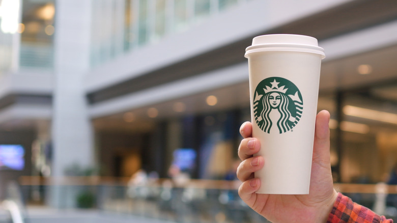 A hand holding a Starbucks cup on a city street