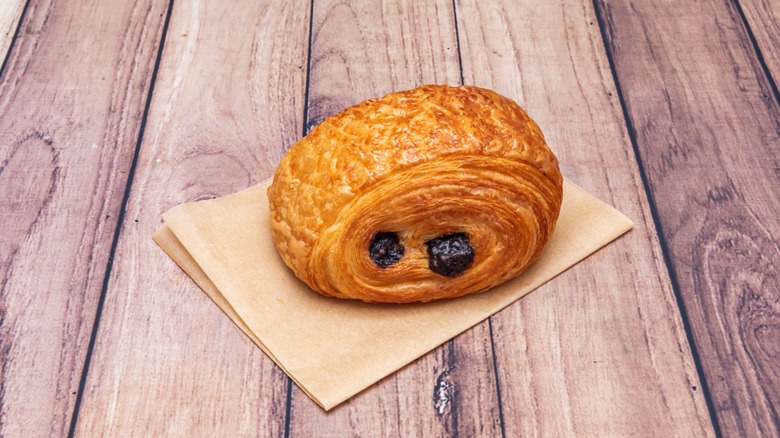 A chocolate croissant on a paper napkin, on a wood table.