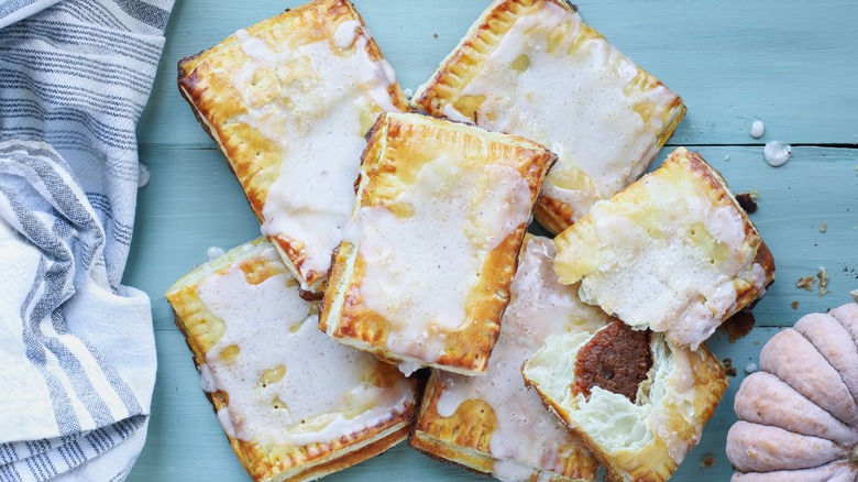 A pile of homemade pop tarts on a wood table, one broken in half to reveal the fruit filling.